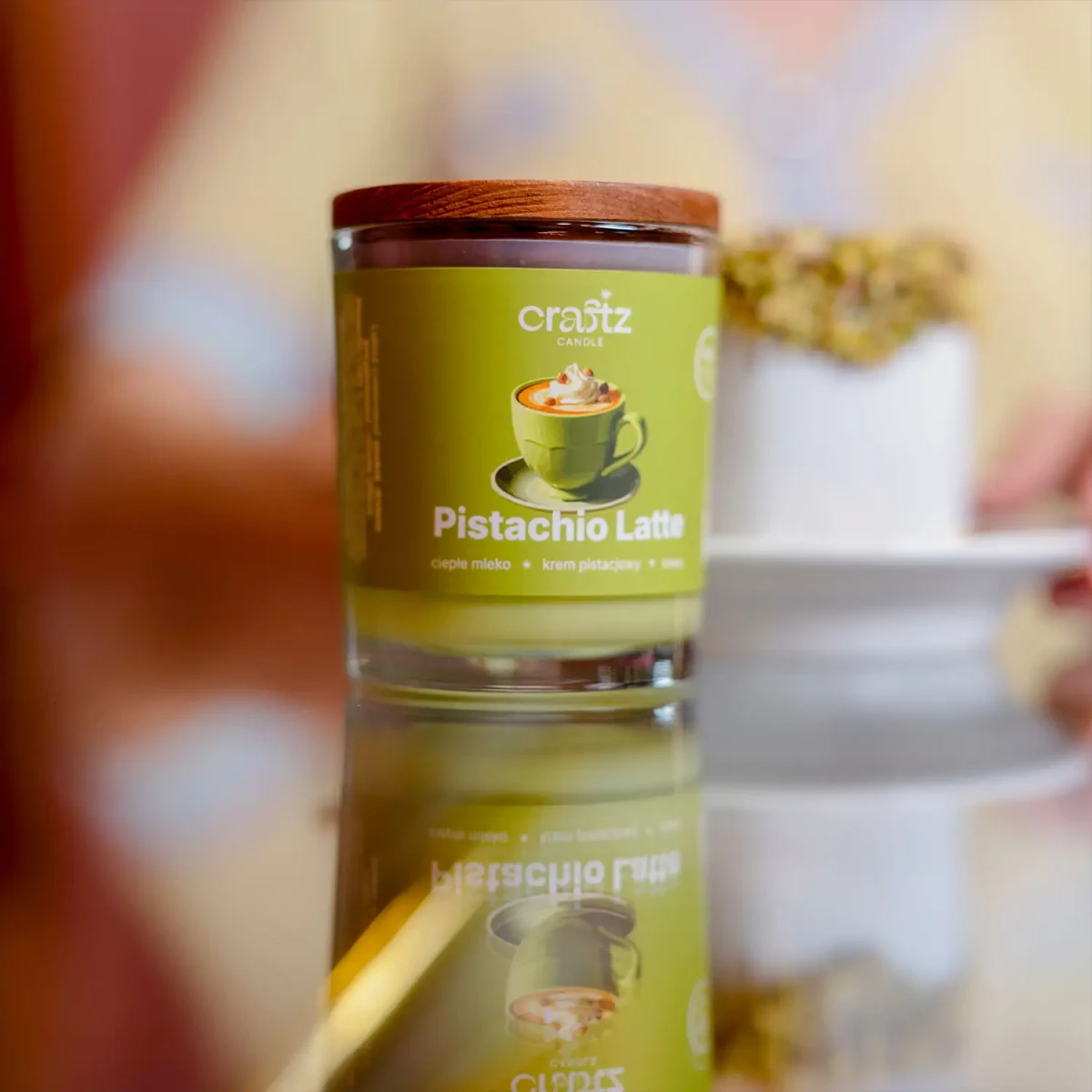 Świeca sojowa Pistachio Latte Craftz Candle na błyszczącej powierzchni z deserem w tle