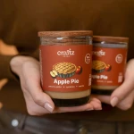 Świeca sojowa Apple Pie Craftz Candle trzymana w dłoniach – druga świeca w tle